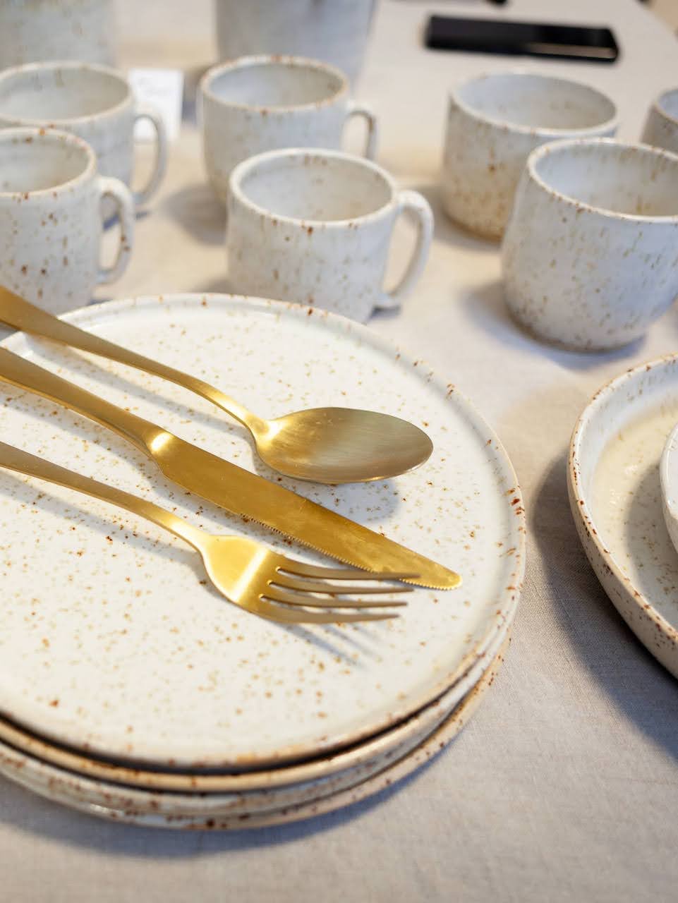 serviesset in spikkelklei met gouden bestek door Atelier KROM Sara Dejonghe